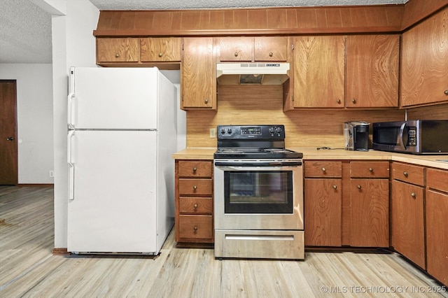 kitchen with under cabinet range hood, light wood-type flooring, light countertops, appliances with stainless steel finishes, and a textured ceiling