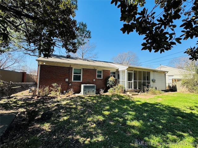 rear view of house with a sunroom, fence, central AC unit, brick siding, and a lawn