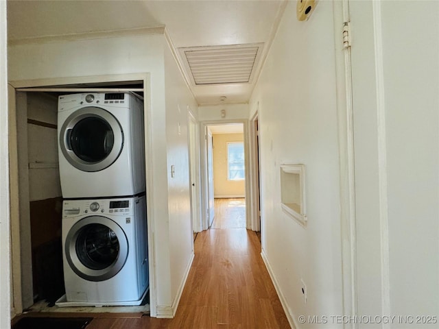 laundry area featuring baseboards, visible vents, stacked washer / dryer, laundry area, and wood finished floors
