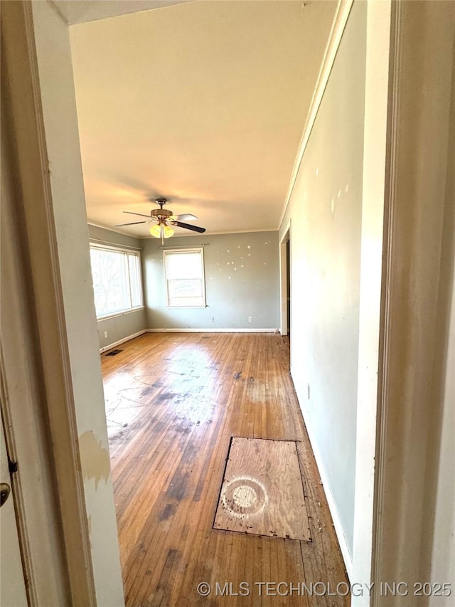 empty room featuring ornamental molding, hardwood / wood-style flooring, baseboards, and ceiling fan