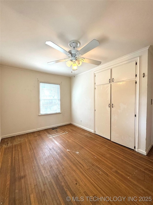 unfurnished bedroom featuring baseboards, a closet, ornamental molding, and hardwood / wood-style flooring