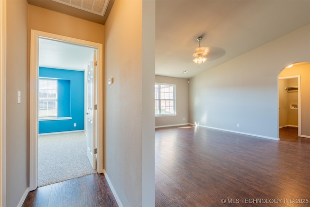 hall with arched walkways, dark wood-style floors, visible vents, and baseboards