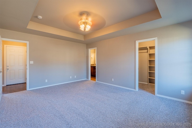 unfurnished bedroom with a walk in closet, baseboards, carpet, and a tray ceiling