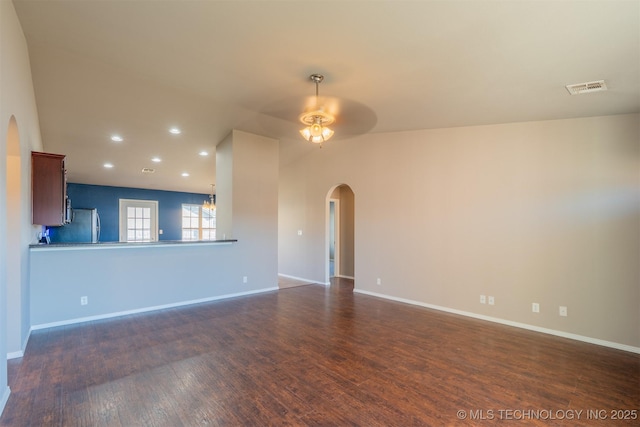 unfurnished living room featuring visible vents, dark wood-type flooring, a ceiling fan, arched walkways, and baseboards