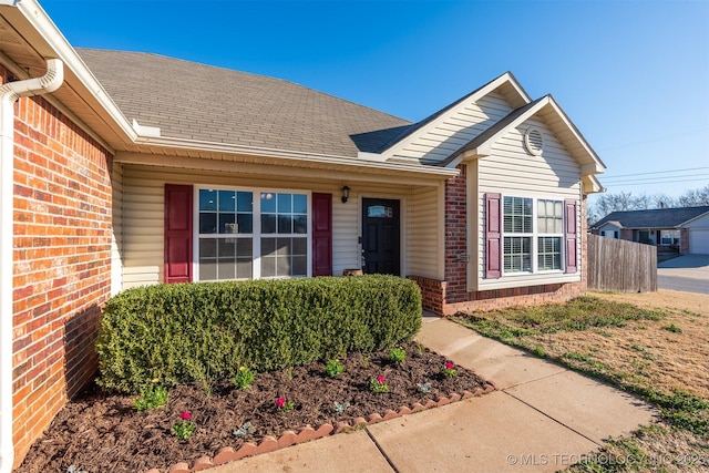 property entrance with brick siding, a shingled roof, and fence