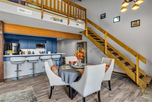 dining area featuring stairs, a high ceiling, wood finished floors, and visible vents