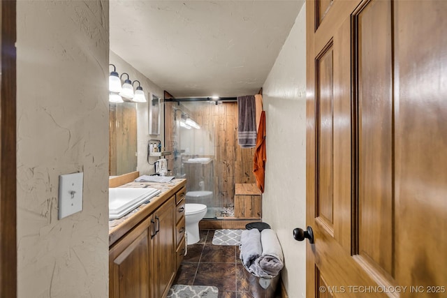 full bathroom with toilet, a stall shower, vanity, and a textured wall