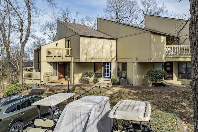 rear view of property featuring central AC unit, a balcony, and roof with shingles