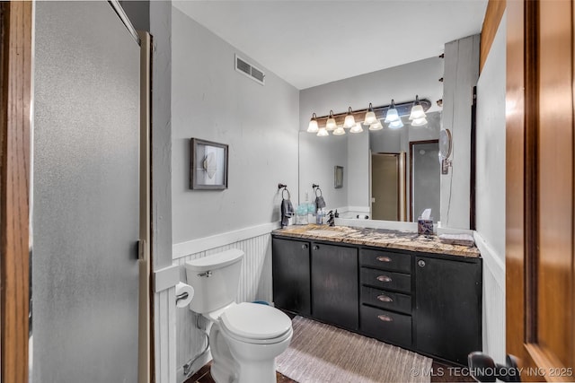 bathroom with vanity, a wainscoted wall, visible vents, an enclosed shower, and toilet