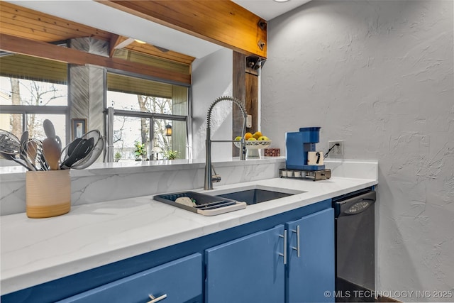 kitchen featuring blue cabinets, light stone counters, a sink, dishwashing machine, and a textured wall