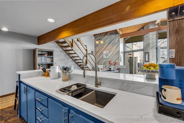 kitchen featuring light stone counters, blue cabinetry, recessed lighting, a sink, and beamed ceiling