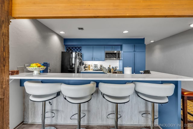 kitchen featuring tasteful backsplash, stainless steel microwave, blue cabinetry, freestanding refrigerator, and built in fridge