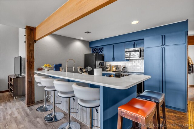 kitchen with blue cabinetry, stainless steel microwave, tasteful backsplash, freestanding refrigerator, and a breakfast bar area