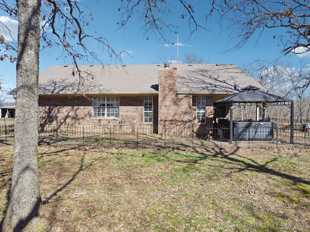 back of house featuring fence, a hot tub, a chimney, a gazebo, and brick siding