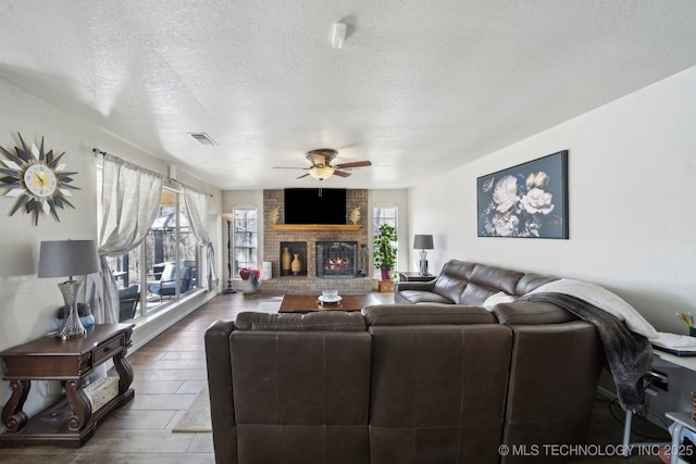 living area featuring visible vents, a brick fireplace, wood finished floors, a textured ceiling, and a ceiling fan