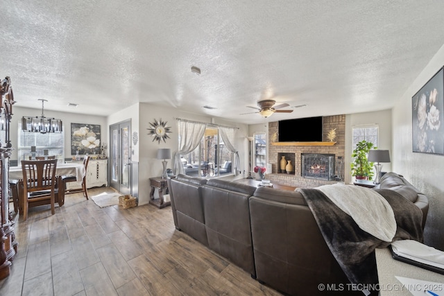 living room featuring a textured ceiling, wood finished floors, a fireplace, and ceiling fan with notable chandelier