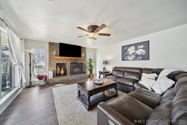 living area featuring a textured ceiling, a brick fireplace, wood finished floors, and a healthy amount of sunlight