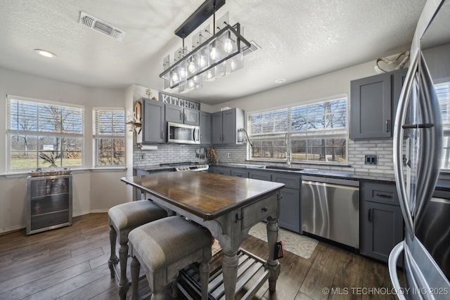 kitchen with dark wood-style floors, visible vents, gray cabinets, a sink, and appliances with stainless steel finishes