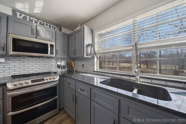 kitchen with a sink, stainless steel appliances, gray cabinets, and dark stone counters