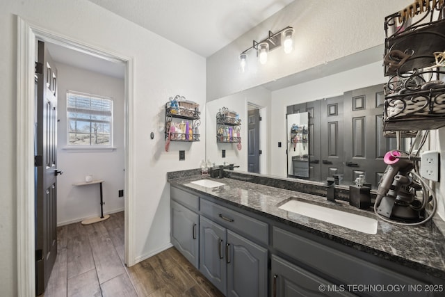 full bathroom featuring double vanity, wood finished floors, baseboards, and a sink