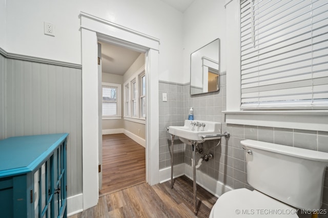 bathroom with a wainscoted wall, toilet, tile walls, and wood finished floors