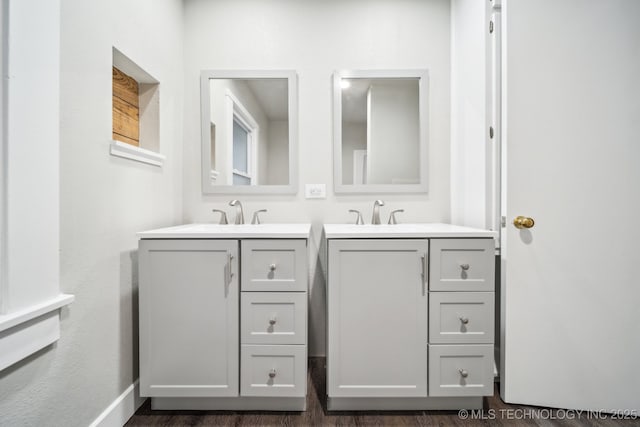 bathroom featuring two vanities, wood finished floors, baseboards, and a sink