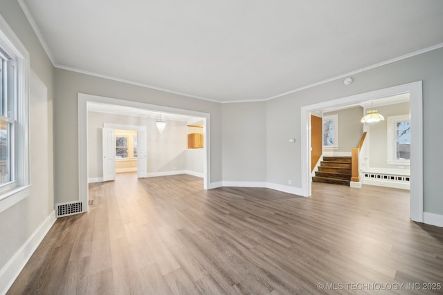 spare room with a wealth of natural light, stairway, wood finished floors, and ornamental molding