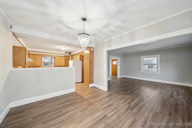 unfurnished living room with a chandelier, baseboards, wood finished floors, and crown molding