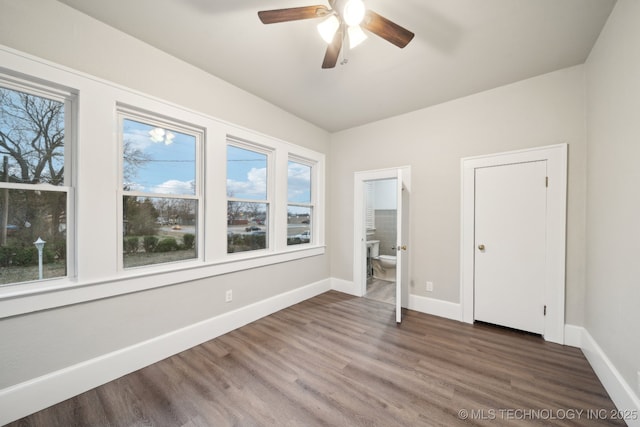 unfurnished bedroom featuring a ceiling fan, ensuite bathroom, baseboards, and wood finished floors