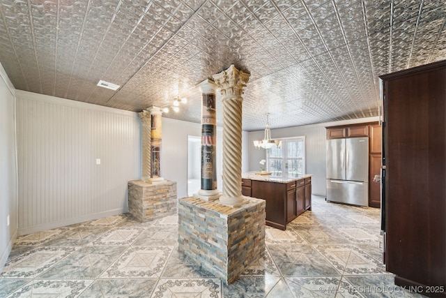 kitchen with visible vents, decorative columns, light stone counters, freestanding refrigerator, and an ornate ceiling