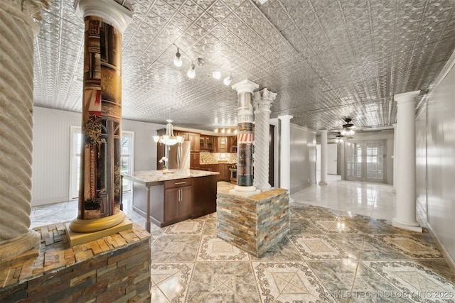 kitchen featuring ornate columns, an ornate ceiling, glass insert cabinets, ceiling fan with notable chandelier, and a center island