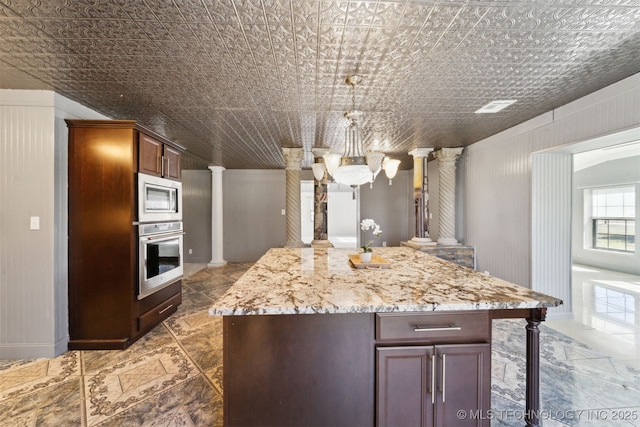 kitchen featuring light stone counters, an ornate ceiling, a center island, appliances with stainless steel finishes, and ornate columns