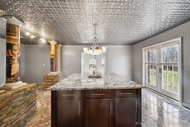 kitchen with dark brown cabinets, light stone countertops, decorative light fixtures, a chandelier, and ornate columns