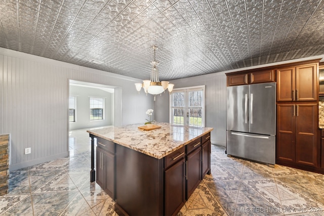 kitchen with a center island, decorative light fixtures, light stone counters, freestanding refrigerator, and an ornate ceiling