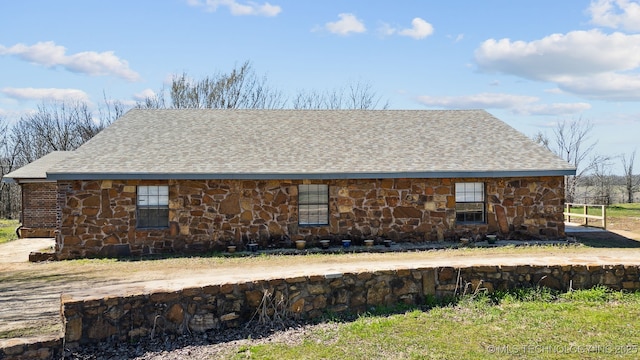 view of side of property featuring stone siding and roof with shingles