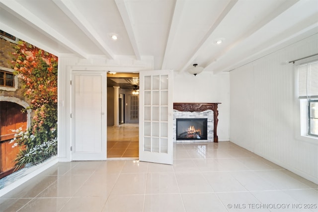 unfurnished living room featuring tile patterned floors, beamed ceiling, and a lit fireplace