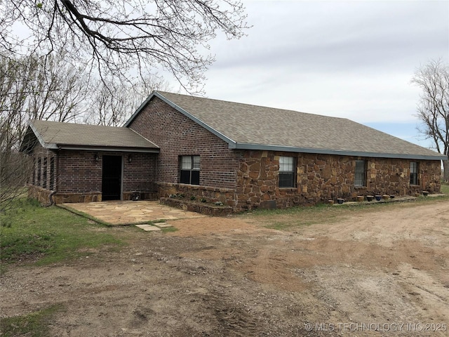 back of property featuring brick siding, stone siding, a patio, and roof with shingles