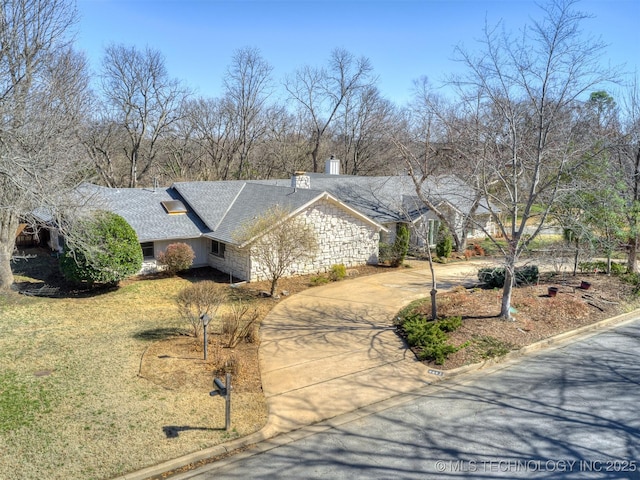 view of front facade featuring a front yard, roof with shingles, a chimney, stone siding, and driveway