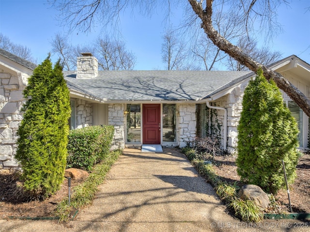 doorway to property featuring stone siding, roof with shingles, and a chimney