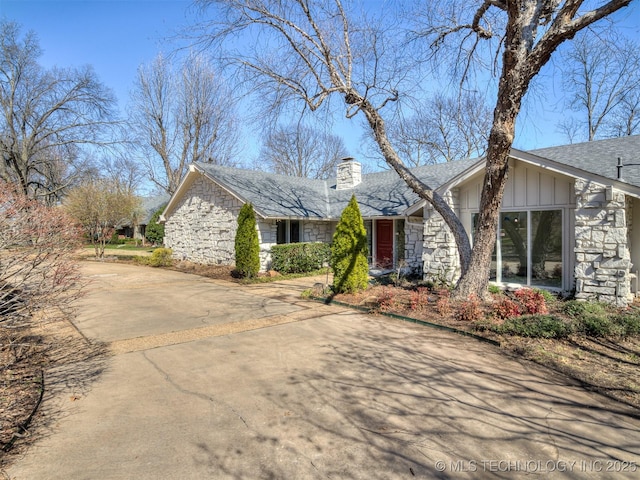 view of front of house with stone siding, driveway, board and batten siding, and a chimney