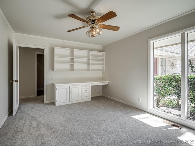 spare room featuring light carpet, built in desk, crown molding, and visible vents