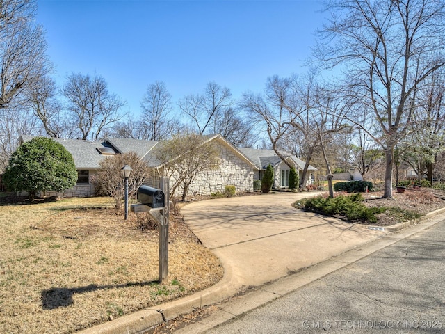 view of front of property with stone siding, roof with shingles, and concrete driveway