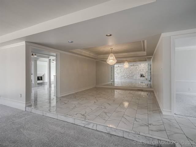 spare room featuring baseboards, ornamental molding, a fireplace, marble finish floor, and a raised ceiling