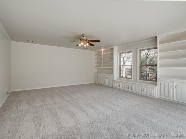 carpeted empty room featuring visible vents, built in shelves, ornamental molding, a ceiling fan, and baseboards