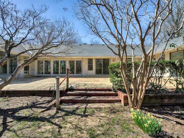 back of property featuring stone siding, roof with shingles, and a patio area