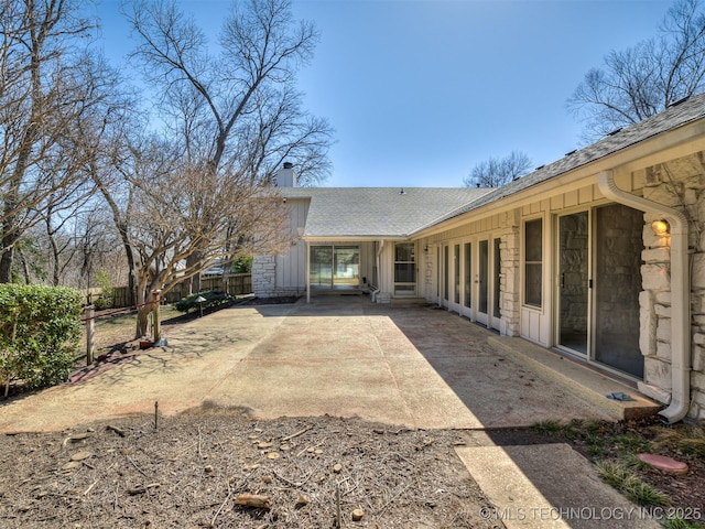 rear view of property with fence, french doors, a chimney, stone siding, and a patio