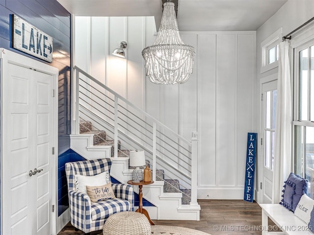 foyer entrance with stairway, a notable chandelier, wood finished floors, and a decorative wall