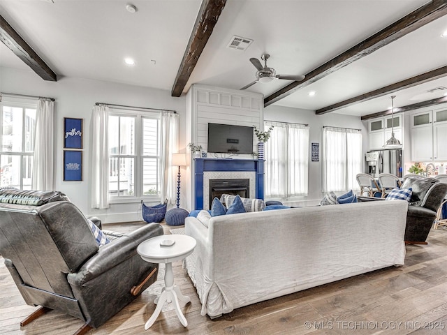 living area with a ceiling fan, wood finished floors, visible vents, beam ceiling, and a fireplace