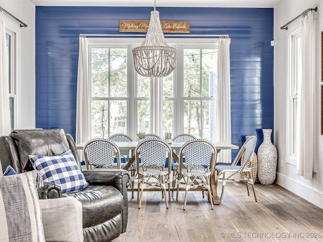 dining area featuring an inviting chandelier, wooden walls, and wood finished floors