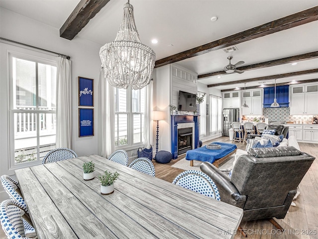 dining area featuring light wood finished floors, visible vents, beam ceiling, ceiling fan with notable chandelier, and a fireplace